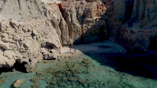 A couple of men and woman walks at the Tsigrado Beach Milos Greece where turquoise waters meet striking rock formations. Witness tranquility and natural beauty in the Cyclades paradise under the sun