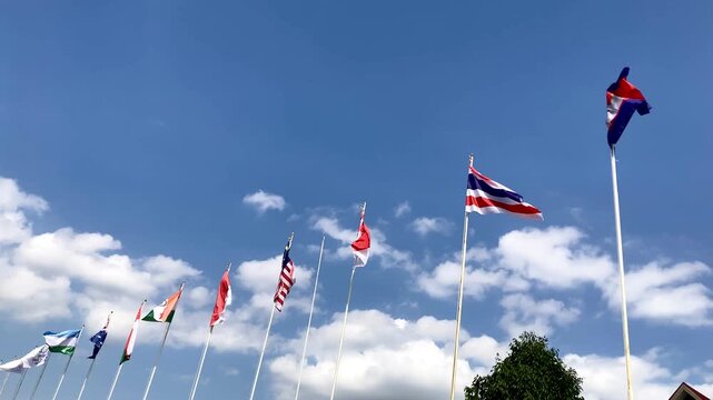 various international country flags flying on tall flagpoles against a blue sky