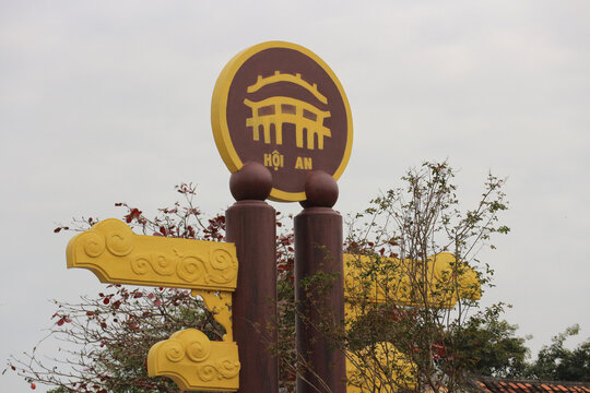 HOI AN, VIETNAM - JANUARY 25, 2026: A close-up, angled view of a sculptural composition featuring the iconic symbol of Hoi An town, framed by tree branches under a cloudy sky.