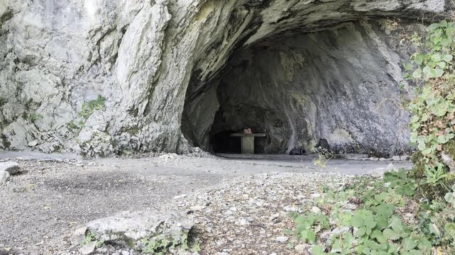 Grotta naturale con ingresso roccioso, pavimento ghiaioso e struttura in pietra interna, circondata da vegetazione verde