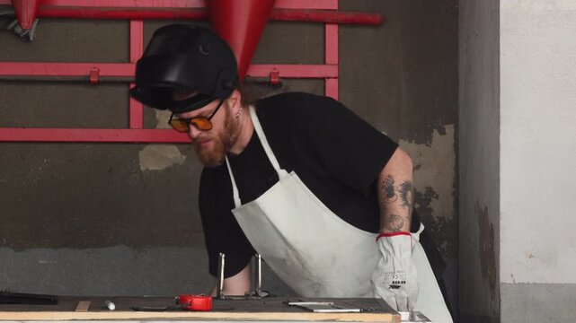 Selective focus on man using physical force to manually deform a heavy steel tube in a workshop