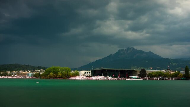 Dramatic stormy time lapse of Mount Pilatus and KKL Lucerne across Lake Lucerne with dark rushing clouds over the Swiss Alps landscape in Switzerland