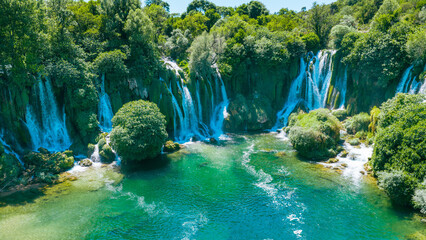 Majestic cascading waterfall surrounded by lush green forest and crystal clear emerald water © Sanja