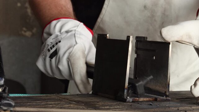 Welder in safety gloves scrubbing freshly welded metal joint using wire scratch brush