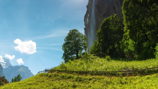 Lauterbrunnen, Switzerland - June 26, 2026: Dynamic time lapse of the iconic Staubbach Falls cascading down a massive cliff face in the Lauterbrunnen Valley. Rushing clouds pass over the bright blue s