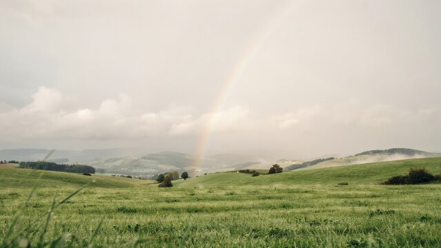Green rolling hills with a rainbow arching over a misty valley landscape with view grassy hills pastoral scene