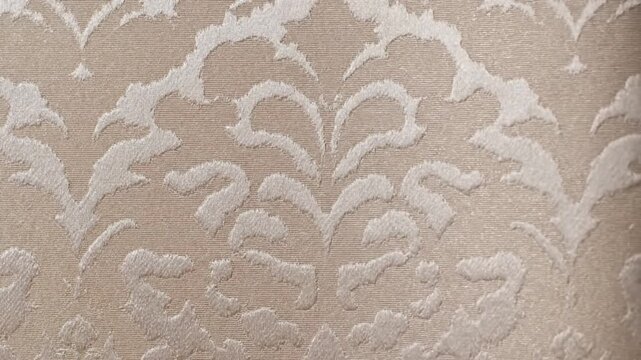 Close up view of beige fabric with floral damask pattern in soft lighting.