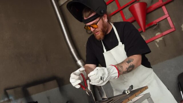 Bearded metalworker in protective gloves using locking pliers to bend a steel plate