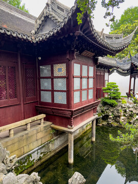 Traditional Chinese wooden pavilion on stilts over a pond with green trees and rocks in Yu Garden, Shanghai, China