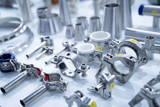 Stainless steel pipe fittings, clamps, and connectors arranged in industrial. Precision manufacturing, mechanical assembly, and hygienic processing systems for food and pharmaceutical industries.