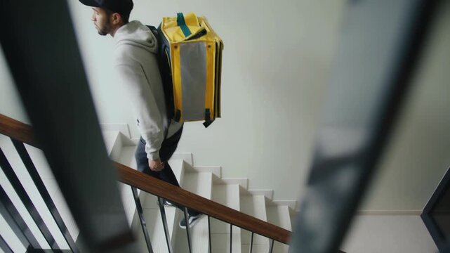 Close view of courier descending stairwell with bright yellow food delivery backpack