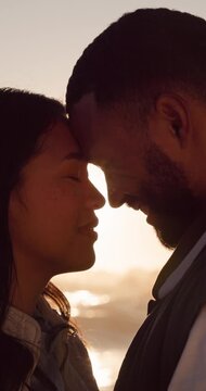 Sunset, couple and love at beach with connection, care or smile for bonding together on outdoor date. Flare, happy people and forehead touch by ocean with romantic relationship, peace and evening.