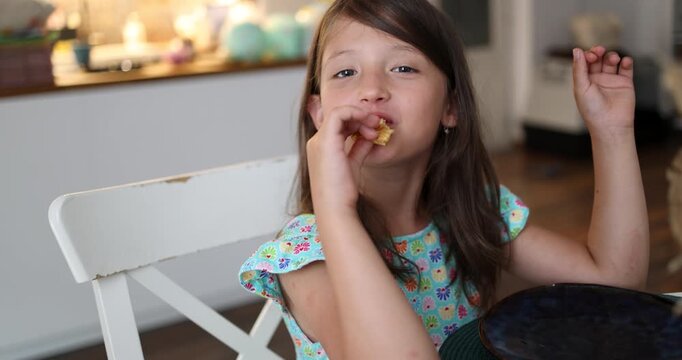 Happy Little Girl Eating Healthy Snack at Home. Joyful Child Enjoying Breakfast in Bright Kitchen