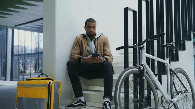 Delivery man waiting seated beside bicycle and insulated bag in modern lobby