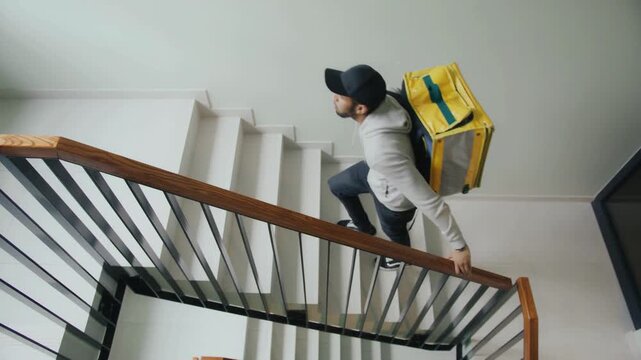 Delivery rider climbing apartment stairs carrying large yellow thermal backpack