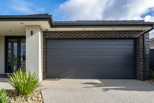 A&nbsp;dark grey sectional double garage door, an aggregate concrete driveway,&nbsp;a rendered portico pillars section of a modern contemporary home in a new housing estate in Austraila