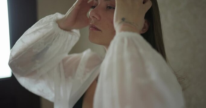Close up of a young woman in white sheer robe raising her hands to her hair