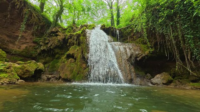 Freshwater cascades down mossy rocks into a tranquil pool. Sokobanja, Serbia.
