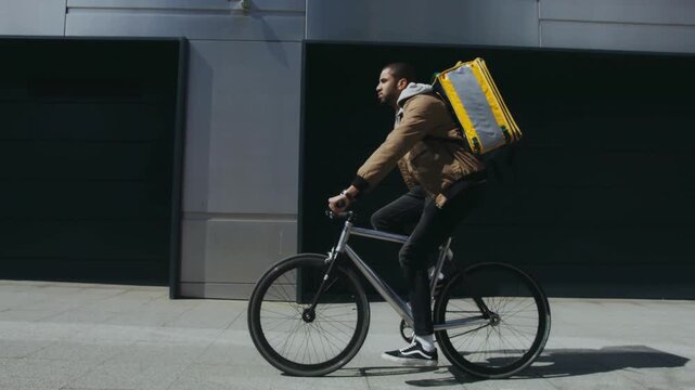 Food delivery cyclist riding fast through urban street with yellow backpack
