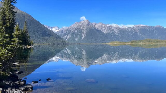 Static slow motion pan of mountain lake reflecting peaks with trees on shoreline in alpine valley
