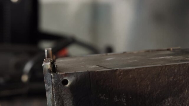 Craftsman holding steel plate edge with metal pliers tool on dark workbench