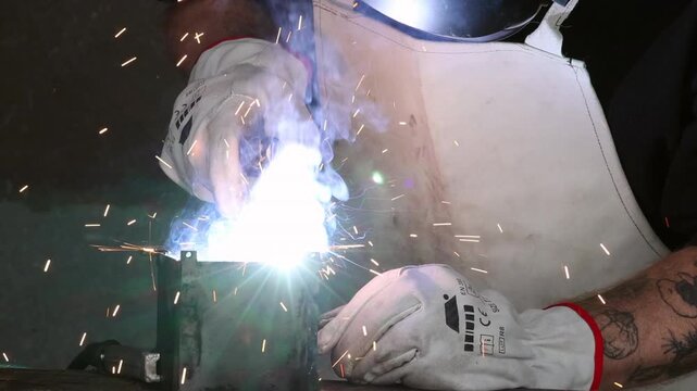 Close up of a craftsman holding welding torch over metal workpiece with blue smoke and sparks