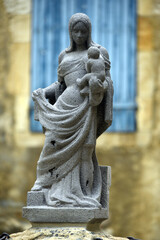 Fototapeta premium Gray lava stone statue of the Virgin Mary holding the Child Jesus in a peaceful inner courtyard. Religious sculpture representing Christian faith, spirituality, devotion and historic heritage 