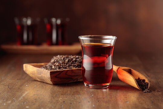 Glass transparent cup of black tea and dry tea in old wooden dish.