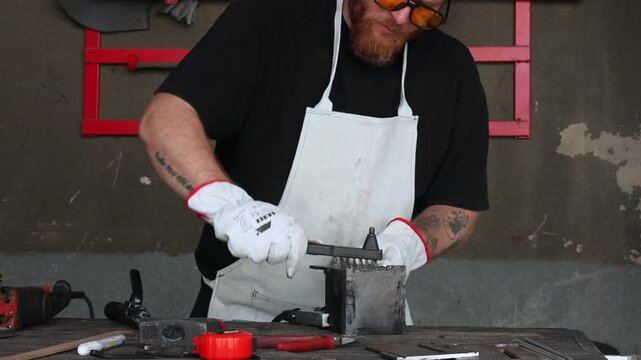 Craftsman in protective gear and mask working with welding tool on steel component