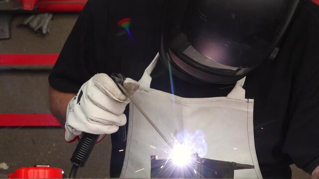 Craftsman in protective gear and mask working with welding tool on steel component