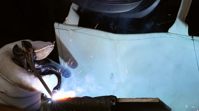 Close up of a man in safety gloves holding electrode holder with flying sparks and smoke