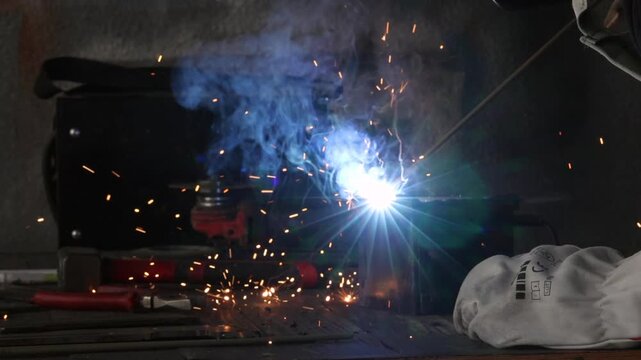 Close up shot of a welder hand igniting arc on metal pipe with bright sparks and smoke.