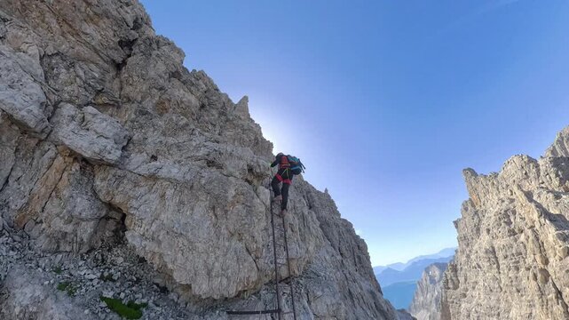 Hiker climbing a steel ladder at Bocca Alta di Massod&igrave; on Via Ferrata Bocchette Alte, Brenta Dolomites