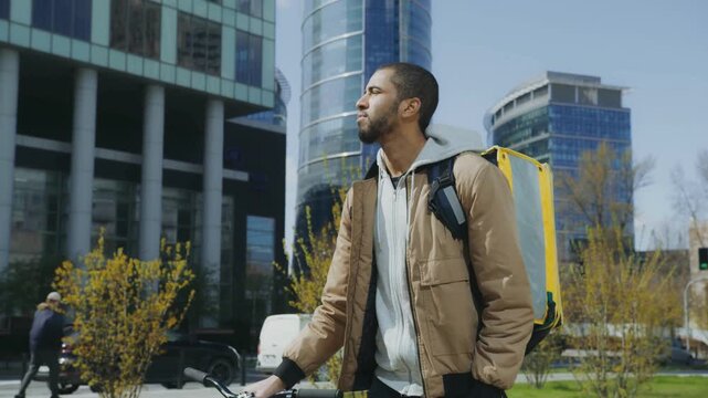 Courier with backpack looking around downtown streets near glass office towers
