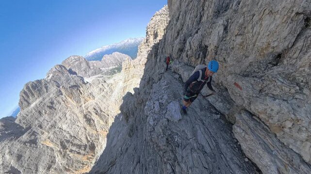 Two hikers crossing an exposed ledge on Via Ferrata Bocchette Alte overlooking the Brenta Dolomites