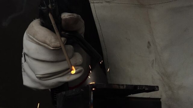Close up shot of a welder hand igniting arc on metal pipe with bright sparks and smoke.