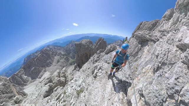 Two hikers crossing an exposed mountain ledge on Via Ferrata Bocchette Alte in the Brenta Dolomites