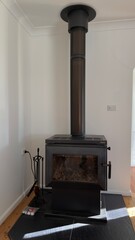 Obraz premium Modern Black Wood Burning Stove with Tall Flue in White Room