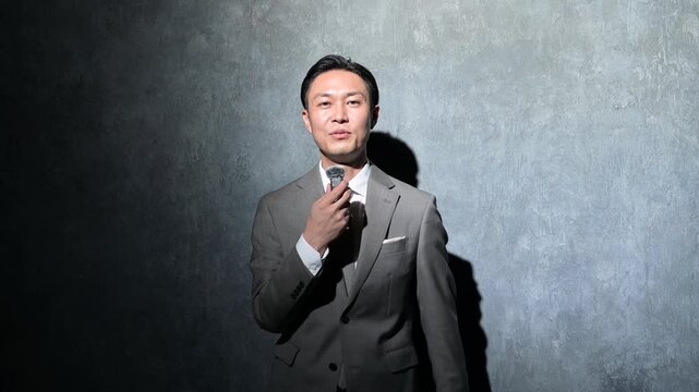 グレー背景で笑顔でプレゼンをする日本人男性