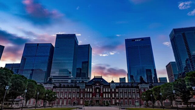 早朝の東京駅周辺の高層ビル街の背景に広がる朝焼け空（丸の内行幸通りから八重洲方面を臨むタイムラプス映像）