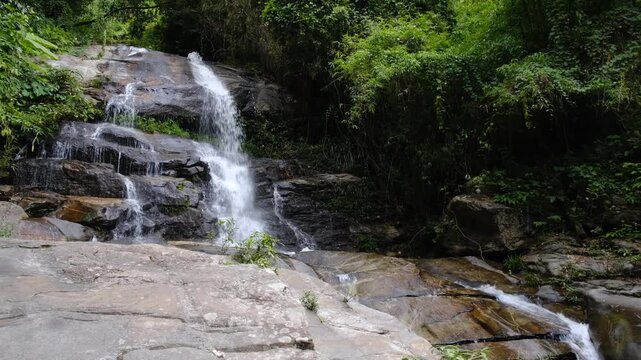 Tropical waterfall cascading over rugged dark rocks in a lush natural forest setting. Perfect for relaxation and nature themes.