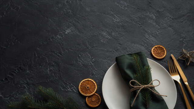 Festive Christmas table setting with white plate, golden cutlery and orange slices on black slate background - Weihnachten- Heiligabend - Weihnachtsfest  - Christmas - Xmas / X-mas - Navidad