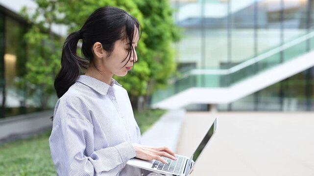 オフィス街でノートパソコンを使って仕事をする30代の日本人ビジネスパーソンの女性