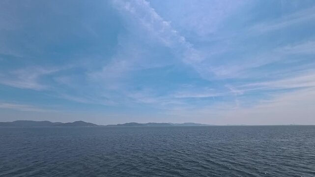 Cinematic real-time video of a beautiful contrail cloud in the blue sky over the calm ocean