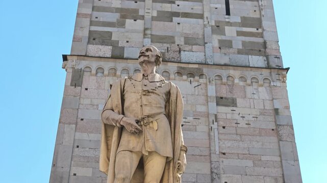 Ghirlandina tower: the resplendent bell tower of Modena cathedral rises under the Italian sky, flanked by the eminent statue of Alessandro Tassoni by the sculptor Alessandro Cavazza from 1860 in