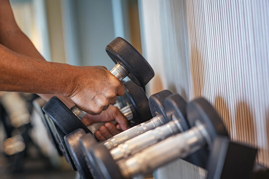 Close-up of hand gripping dumbbell on chrome rack in modern gym, symbolising strength training, physical longevity and muscle recovery for active healthy lifestyle and fitness motivation daily