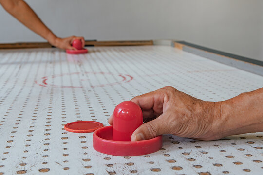 Hand placing on air hockey pusher to push red round puck on table for casual indoor game with friends, showing social recreation, mindful leisure play, screen-free home analog entertainment activity