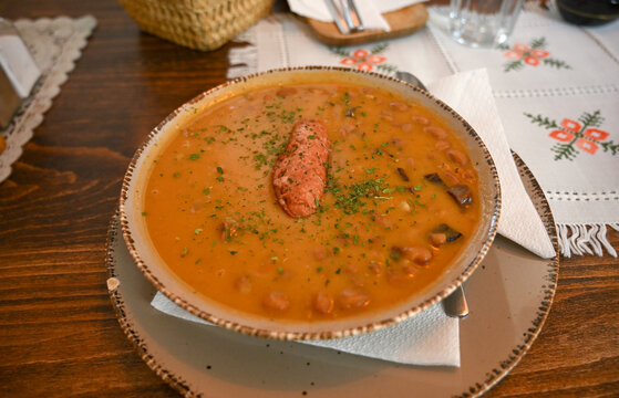 Traditional bean stew with meat and sausage served in a plate at a restaurant.