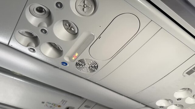 Airplane cabin ceiling with overhead panel, reading lights and air vents, close view of passenger seat area, calm travel atmosphere and modern transport setting