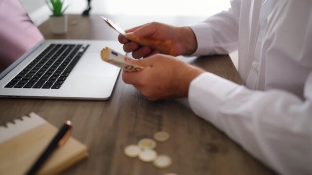 Close-up view of businessman's hands counting fifty euro banknotes and coins at office desk. Concept successful wealth management, income, and financial savings